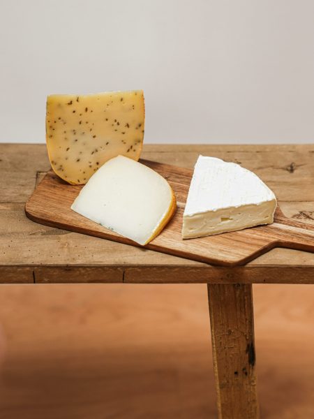 Three types of gourmet cheese displayed on a wooden chopping board, perfect for culinary enthusiasts.